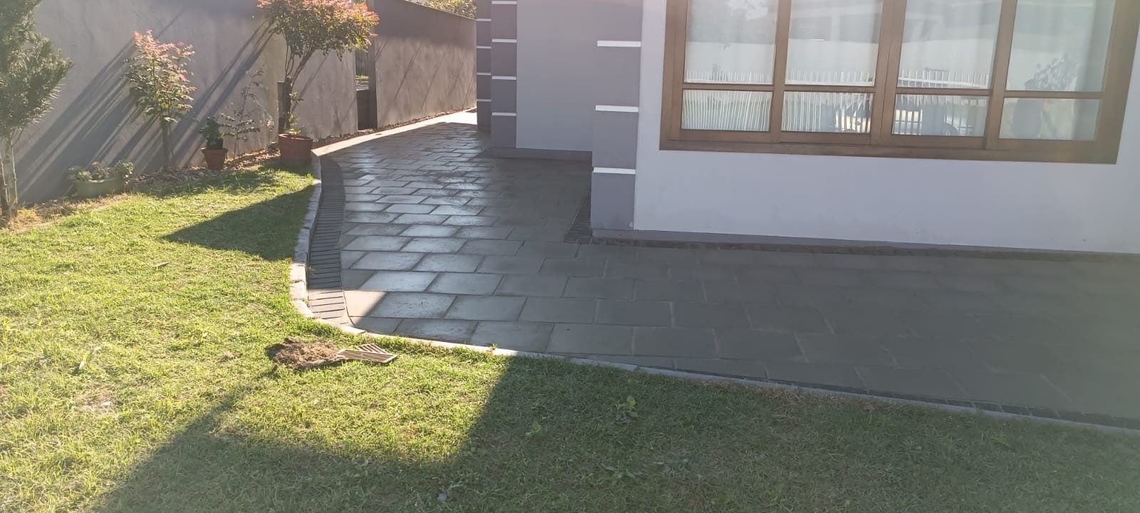 Caminho de pedra escura contornando a casa ao lado da grama