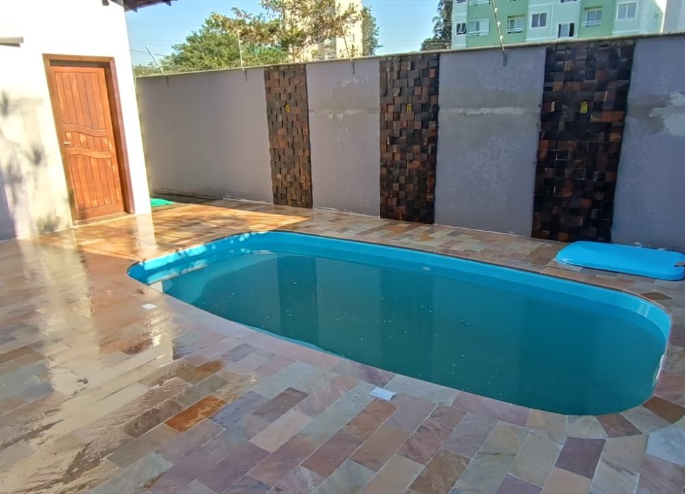 Área de piscina com piso de pedra e muro revestido com filetes de pedra